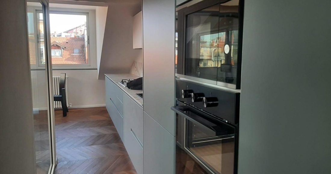 Cucina su misura in un sottotetto, con forno da incasso, piano in marmo e parquet a spina di pesce